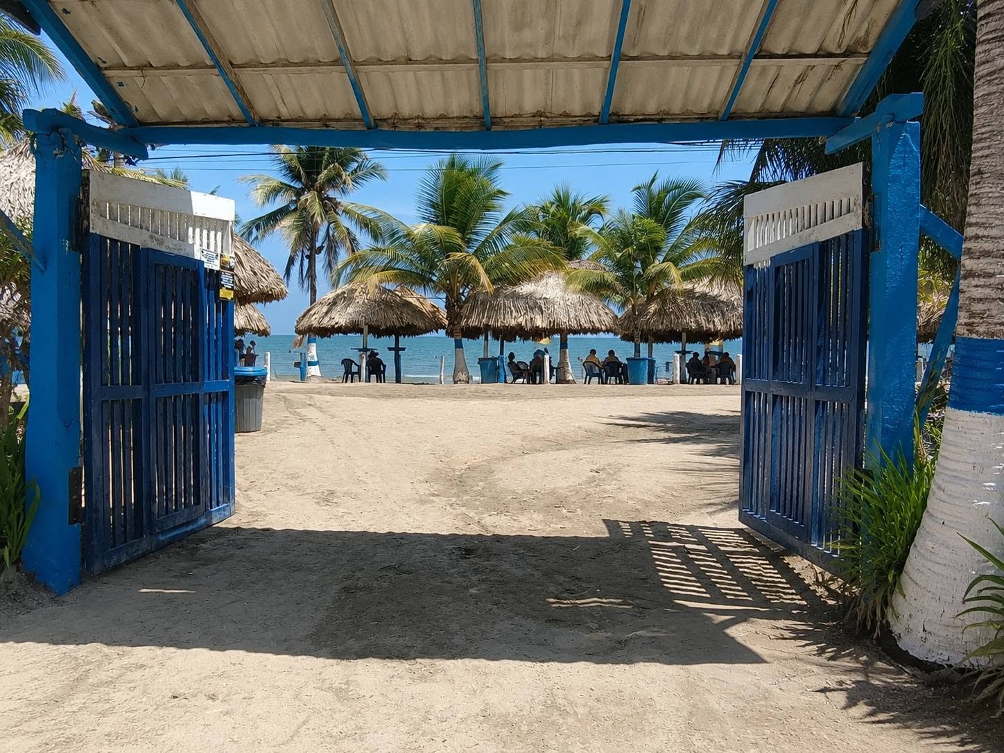 Entrada azul hacia la playa con palmeras y kioscos